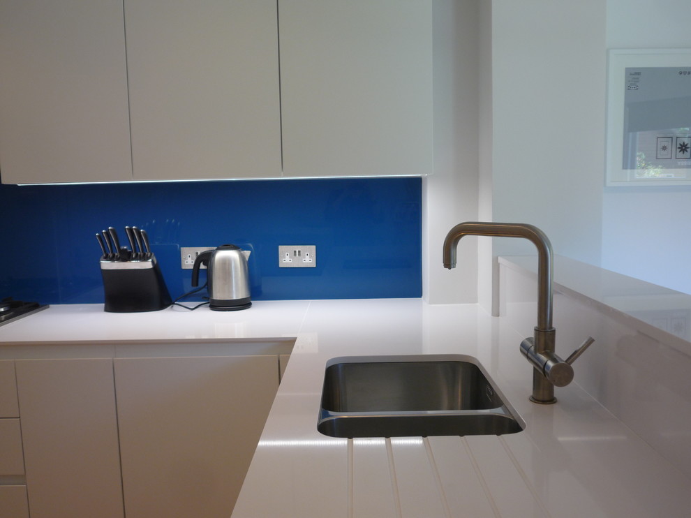 Inspiration for a medium sized modern u-shaped kitchen/diner in London with a submerged sink, flat-panel cabinets, white cabinets, engineered stone countertops, blue splashback, glass sheet splashback, stainless steel appliances, no island and light hardwood flooring.