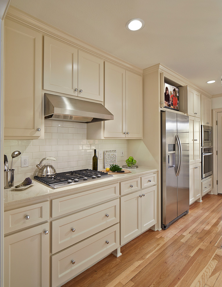 Small traditional galley enclosed kitchen in Dallas with a submerged sink, shaker cabinets, white cabinets, engineered stone countertops, white splashback, metro tiled splashback, stainless steel appliances, light hardwood flooring and no island.
