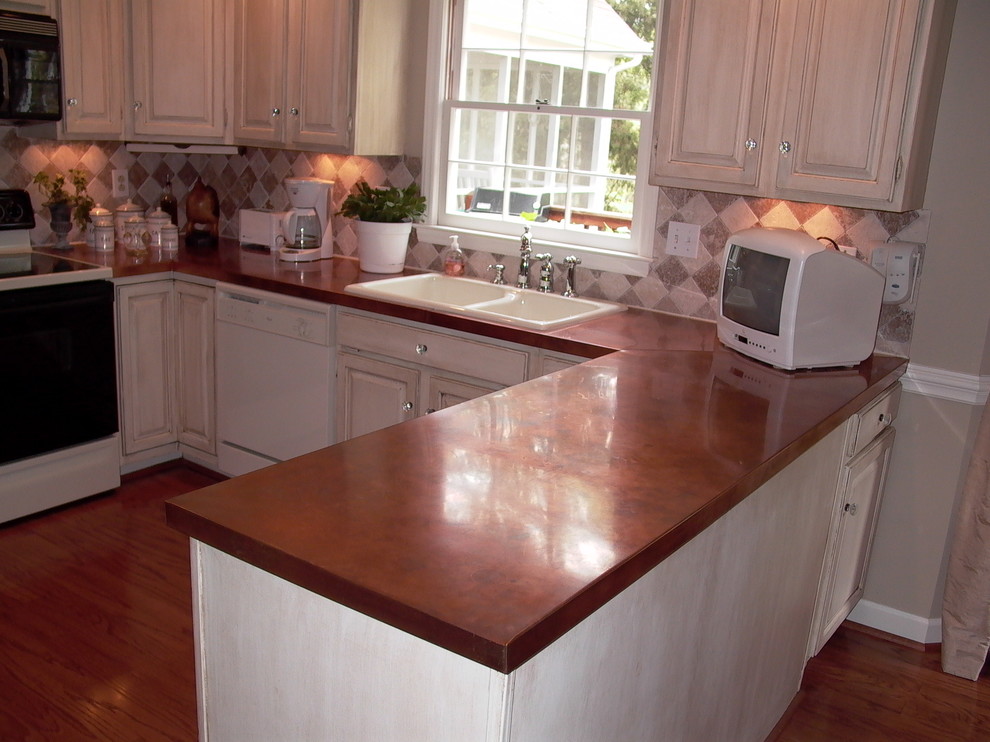Bild på ett amerikanskt kök, med en dubbel diskho, beige stänkskydd, stänkskydd i cementkakel, mellanmörkt trägolv, skåp i slitet trä och bänkskiva i akrylsten