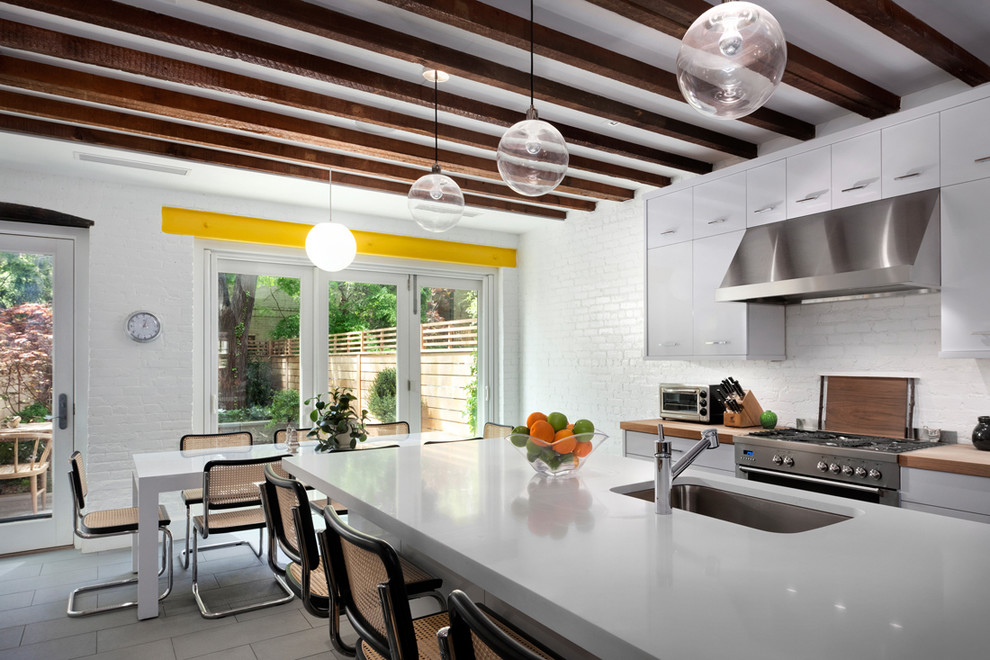 Photo of a large retro single-wall kitchen/diner in New York with a submerged sink, flat-panel cabinets, white cabinets, white splashback, an island, composite countertops, stainless steel appliances and porcelain flooring.