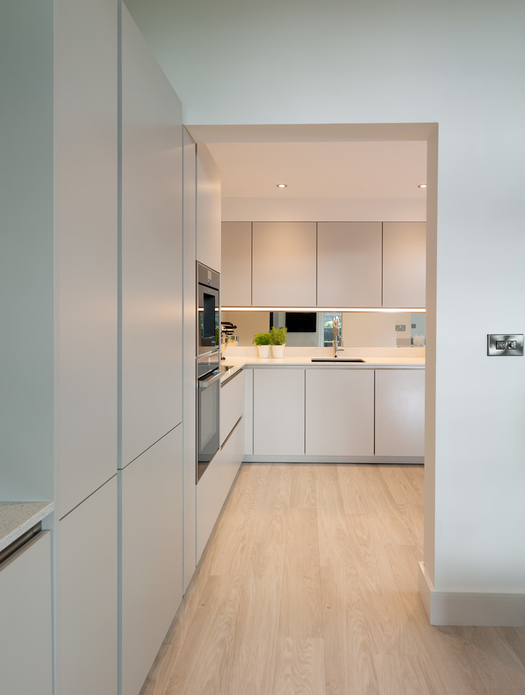 Idée de décoration pour une petite cuisine américaine minimaliste avec un placard à porte plane, des portes de placard grises et un plan de travail en quartz modifié.