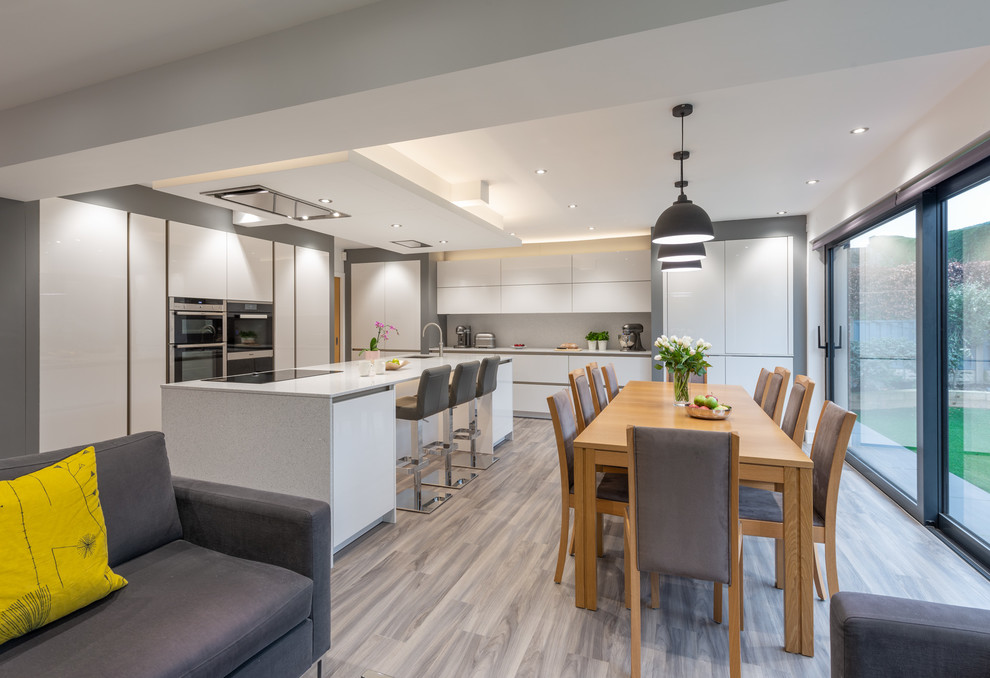 Photo of a medium sized modern kitchen/diner in Other with white cabinets, engineered stone countertops, black appliances, an island, grey floors and white worktops.