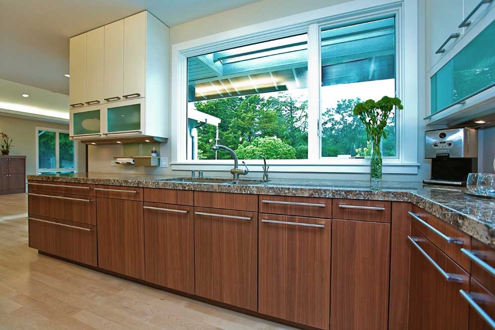 This is an example of a large contemporary u-shaped open plan kitchen in San Francisco with a submerged sink, flat-panel cabinets, granite worktops, white splashback, stainless steel appliances, light hardwood flooring, white cabinets, an island, beige floors and multicoloured worktops.