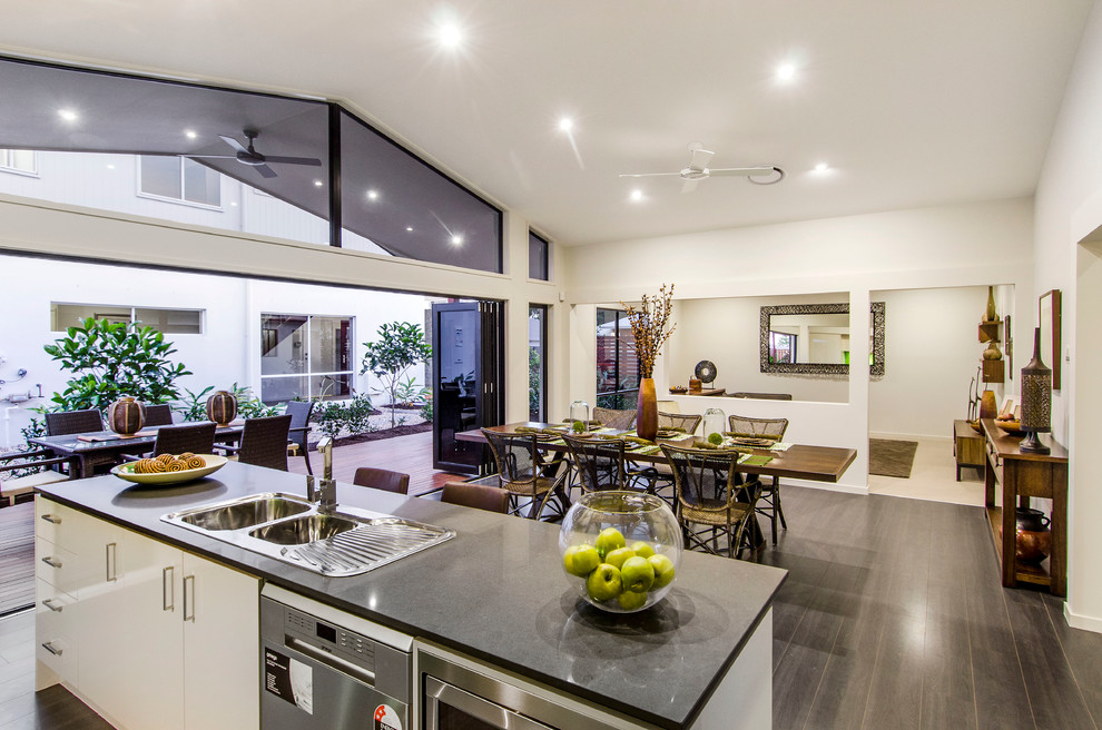 Example of a mid-sized trendy galley vinyl floor eat-in kitchen design in Brisbane with a double-bowl sink, flat-panel cabinets, white cabinets, quartz countertops, green backsplash, glass sheet backsplash, stainless steel appliances and an island