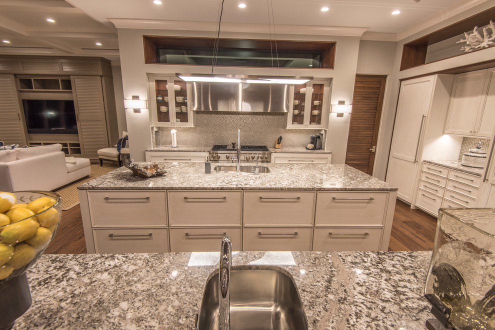 Inspiration for a large tropical u-shaped light wood floor open concept kitchen remodel in Tampa with an undermount sink, shaker cabinets, white cabinets, granite countertops, gray backsplash, glass tile backsplash, paneled appliances and two islands