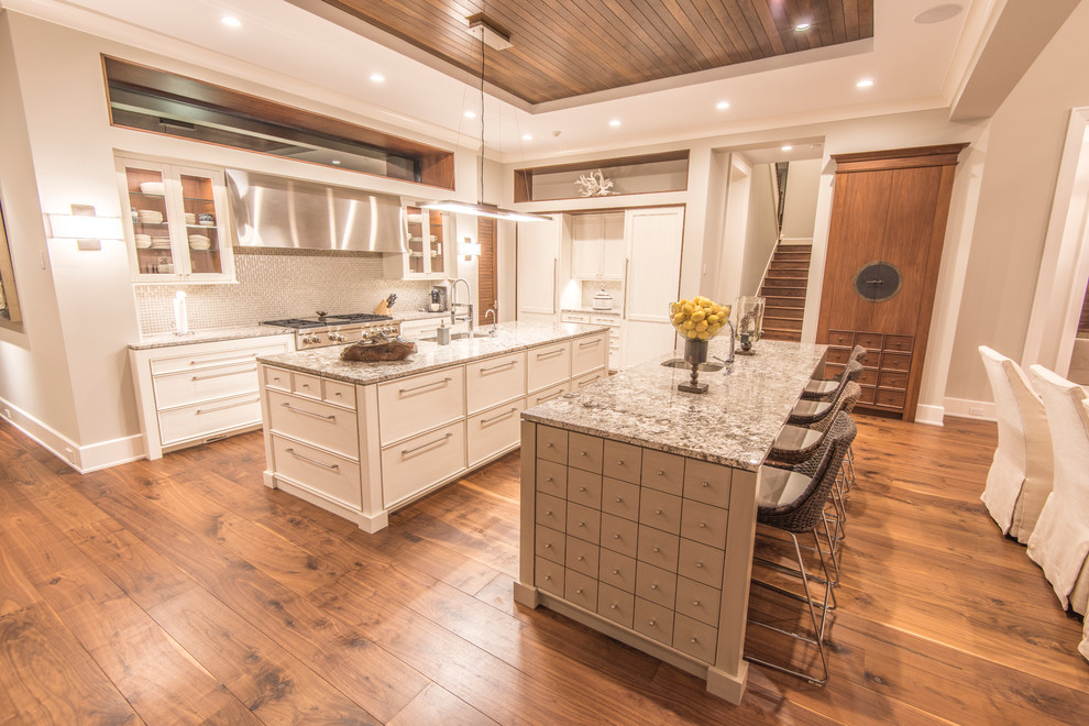 Example of a large island style u-shaped light wood floor open concept kitchen design in Tampa with an undermount sink, shaker cabinets, white cabinets, granite countertops, gray backsplash, glass tile backsplash, paneled appliances and two islands