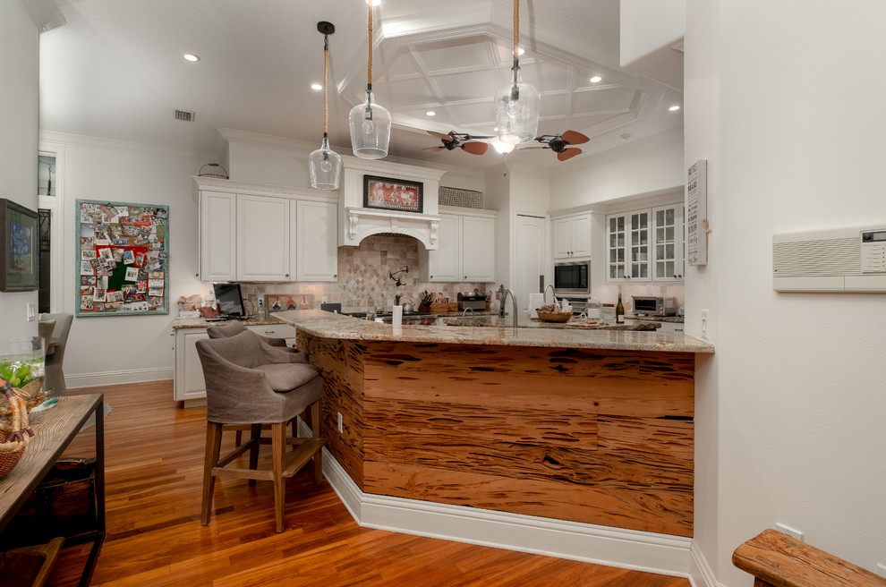 Bild på ett stort maritimt brun brunt kök, med en nedsänkt diskho, luckor med upphöjd panel, vita skåp, granitbänkskiva, brunt stänkskydd, stänkskydd i trä, rostfria vitvaror, mellanmörkt trägolv, en köksö och brunt golv