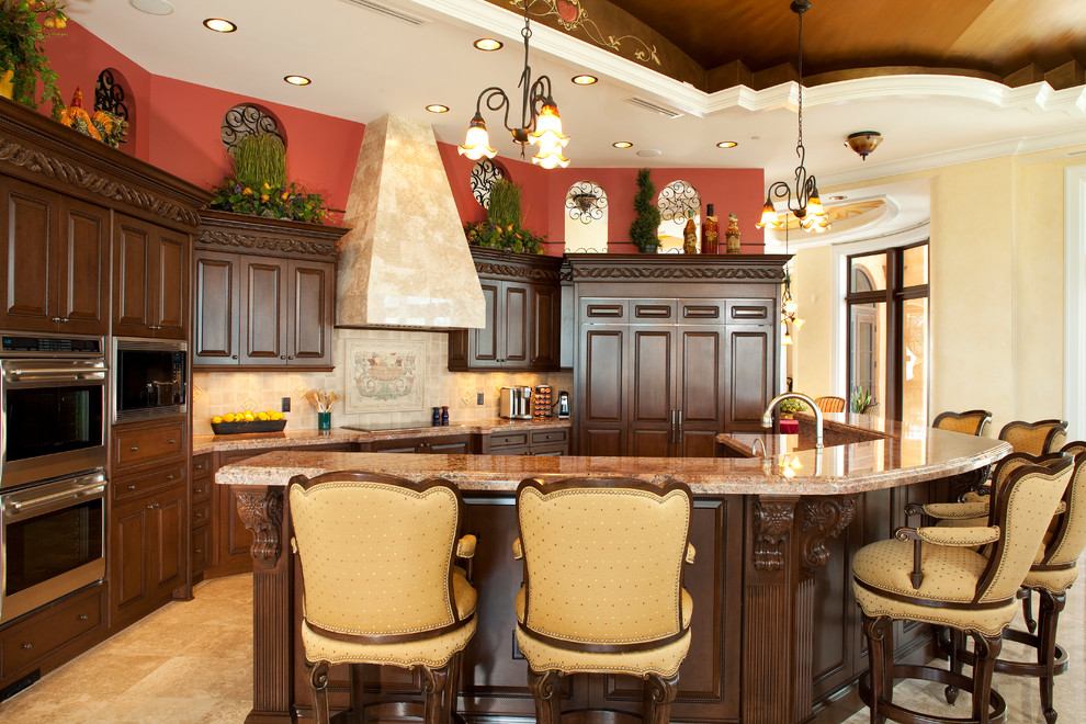 Foto di un cucina con isola centrale mediterraneo con ante con bugna sagomata, ante in legno bruno, paraspruzzi beige e elettrodomestici in acciaio inossidabile