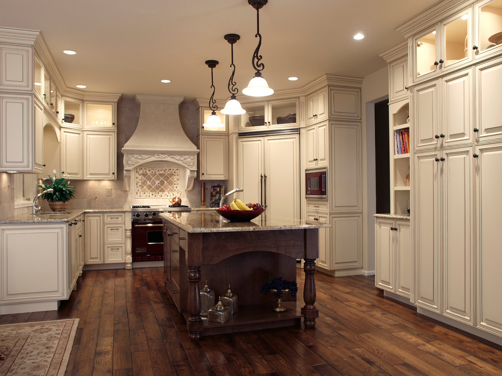 Example of a mid-sized classic u-shaped dark wood floor and brown floor kitchen design in Denver with a double-bowl sink, raised-panel cabinets, beige cabinets, granite countertops, beige backsplash, ceramic backsplash, paneled appliances and an island