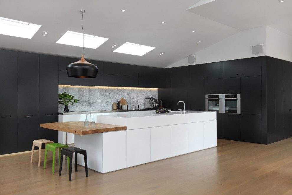 Свежая идея для дизайна: угловая кухня среднего размера в современном стиле с фартуком из каменной плиты, паркетным полом среднего тона, островом и черно-белыми фасадами - отличное фото интерьера