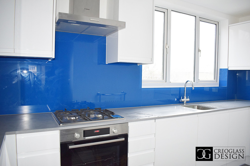 Inredning av ett modernt stort grå grått kök och matrum, med vita skåp, blått stänkskydd och glaspanel som stänkskydd