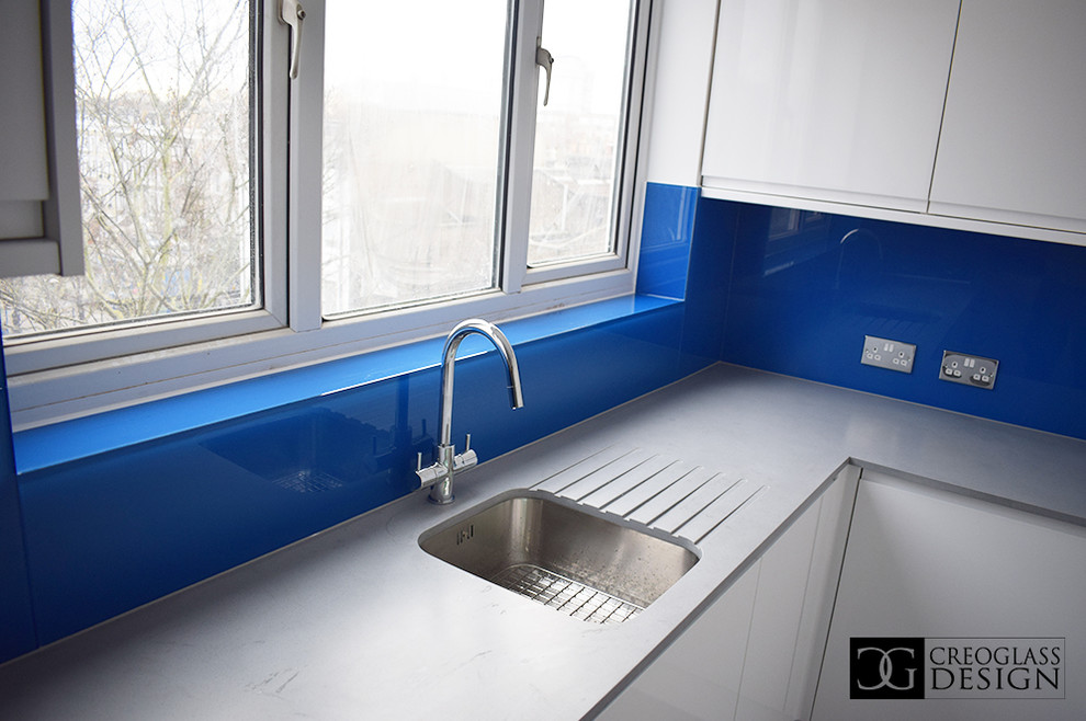 Foto på ett stort funkis grå kök och matrum, med vita skåp, blått stänkskydd och glaspanel som stänkskydd
