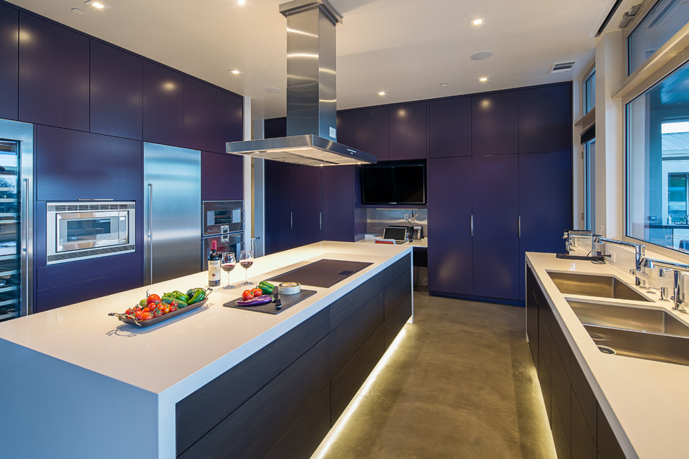 Modern inredning av ett stort kök, med en trippel diskho, släta luckor, blå skåp, bänkskiva i kvarts, rostfria vitvaror, betonggolv och en köksö