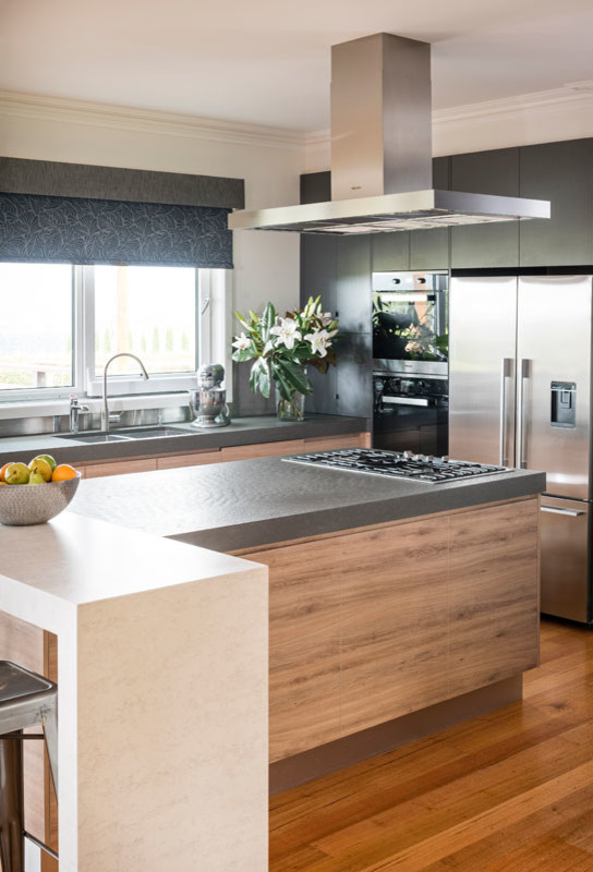 Inspiration for a large industrial l-shaped medium tone wood floor open concept kitchen remodel in Melbourne with an undermount sink, flat-panel cabinets, light wood cabinets, concrete countertops, metallic backsplash, black appliances and an island