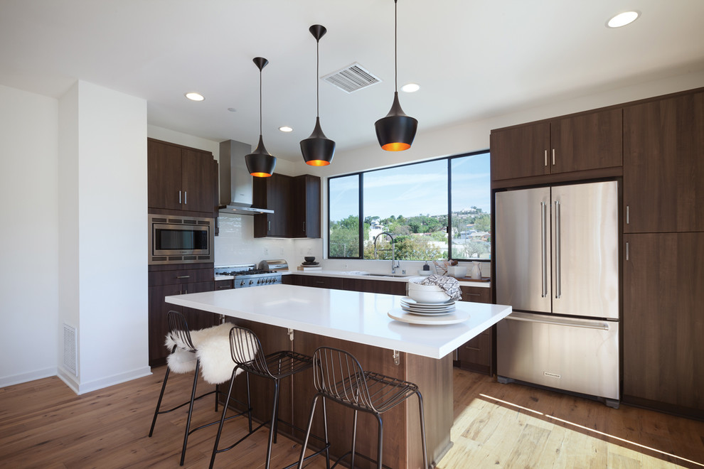 Moderne Küche in L-Form mit flächenbündigen Schrankfronten, Küchenrückwand in Weiß, Küchengeräten aus Edelstahl und Kücheninsel in Orange County