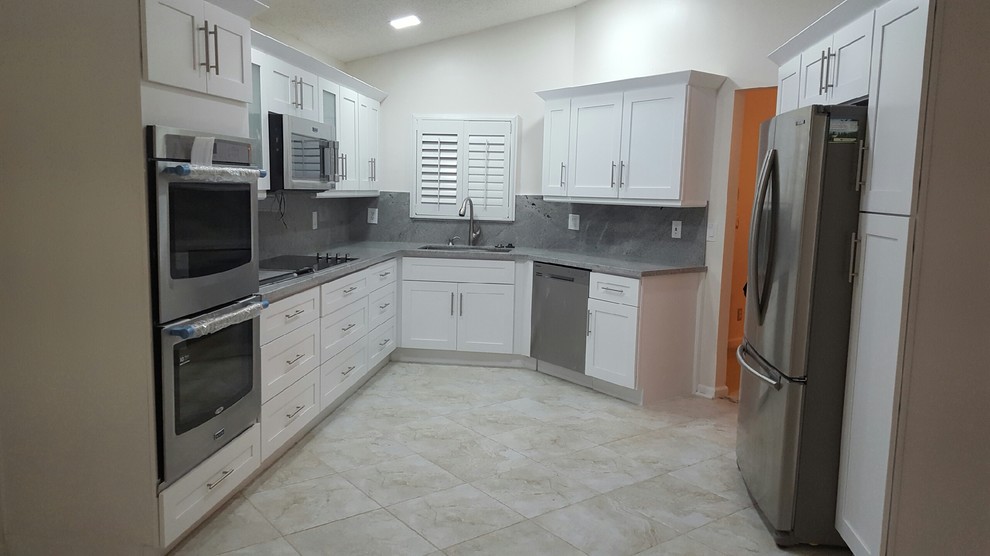 Photo of a medium sized modern u-shaped kitchen/diner in Miami with a double-bowl sink, shaker cabinets, white cabinets, grey splashback, stainless steel appliances, no island and beige floors.