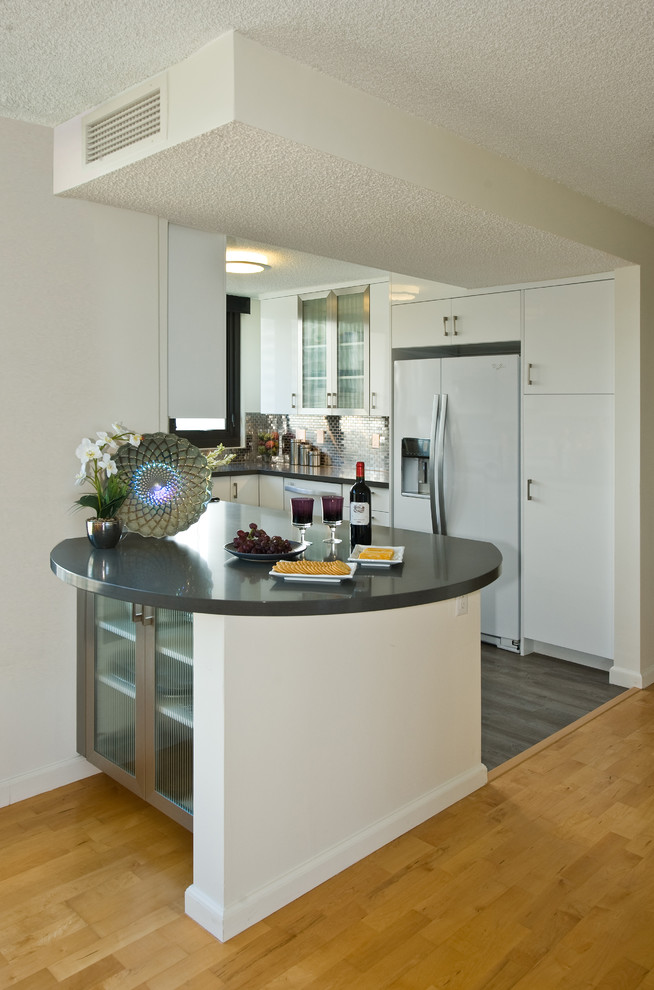 Idéer för att renovera ett funkis kök, med släta luckor, vita skåp, stänkskydd med metallisk yta, spegel som stänkskydd, vita vitvaror och en köksö