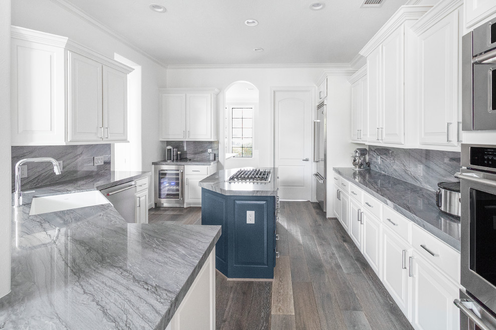 Inredning av ett klassiskt mellanstort grå grått kök, med en rustik diskho, luckor med upphöjd panel, blå skåp, bänkskiva i kvartsit, grått stänkskydd, stänkskydd i sten, rostfria vitvaror, mellanmörkt trägolv, en köksö och grått golv