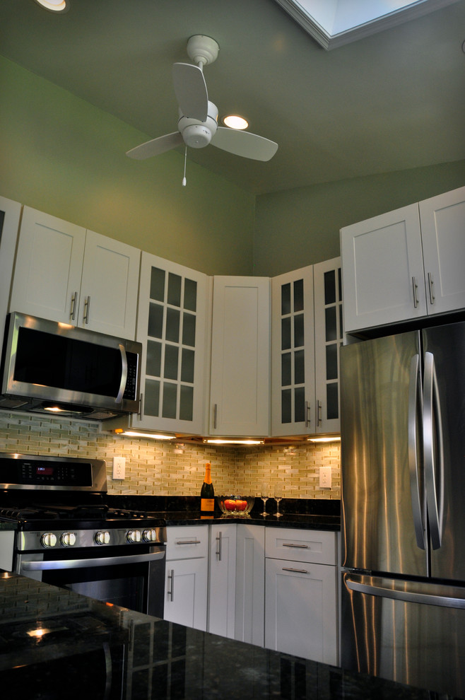 Klassisk inredning av ett mellanstort kök, med en undermonterad diskho, skåp i shakerstil, vita skåp, granitbänkskiva, gult stänkskydd, stänkskydd i glaskakel, rostfria vitvaror, mörkt trägolv och en halv köksö