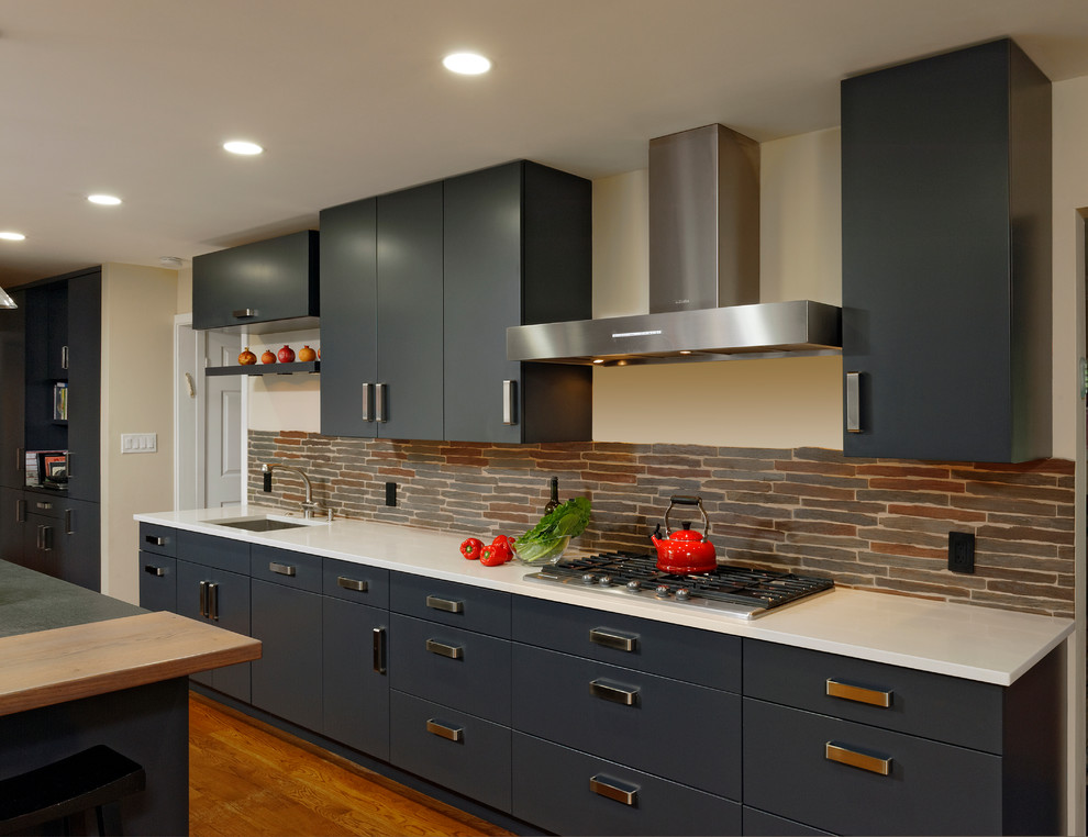 Bild på ett stort funkis kök, med en undermonterad diskho, släta luckor, grå skåp, granitbänkskiva, grått stänkskydd, stänkskydd i sten, rostfria vitvaror, ljust trägolv och en köksö