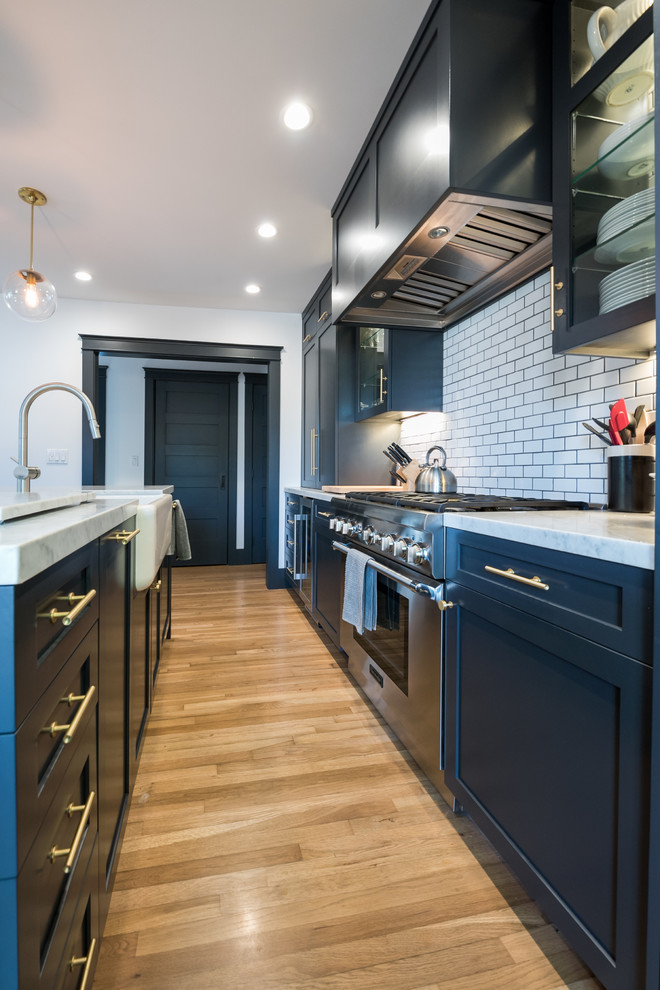This is an example of a medium sized traditional single-wall kitchen/diner in Los Angeles with a belfast sink, shaker cabinets, blue cabinets, marble worktops, white splashback, porcelain splashback, coloured appliances, light hardwood flooring and an island.