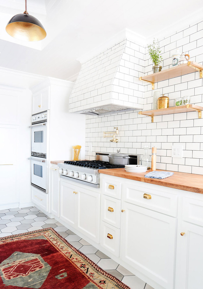 Example of a mid-sized farmhouse u-shaped ceramic tile open concept kitchen design in Los Angeles with a farmhouse sink, recessed-panel cabinets, white cabinets, marble countertops, white backsplash, subway tile backsplash, white appliances and a peninsula