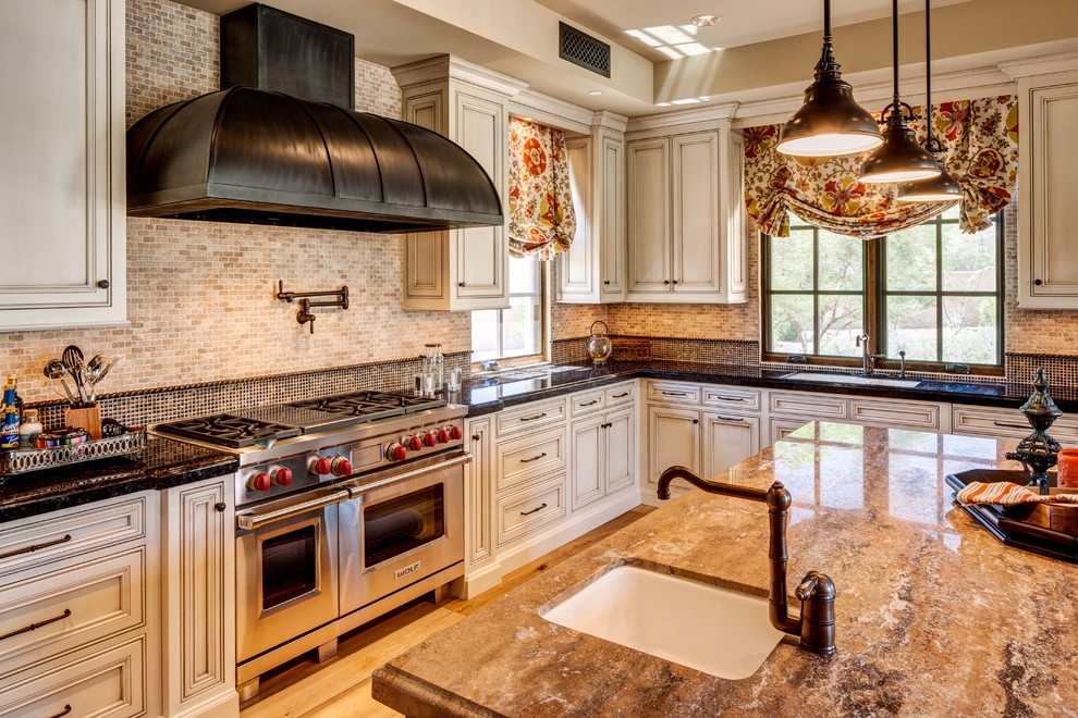 Example of a mid-sized tuscan u-shaped light wood floor and beige floor open concept kitchen design in Phoenix with recessed-panel cabinets, white cabinets, granite countertops, beige backsplash, an undermount sink, mosaic tile backsplash, stainless steel appliances, an island and brown countertops