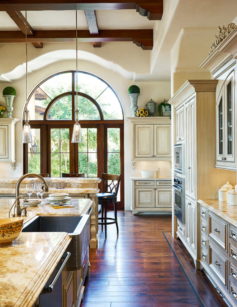 Inspiration for a large mediterranean u-shaped dark wood floor open concept kitchen remodel in Phoenix with a farmhouse sink, raised-panel cabinets, granite countertops, two islands, beige backsplash, ceramic backsplash and stainless steel appliances