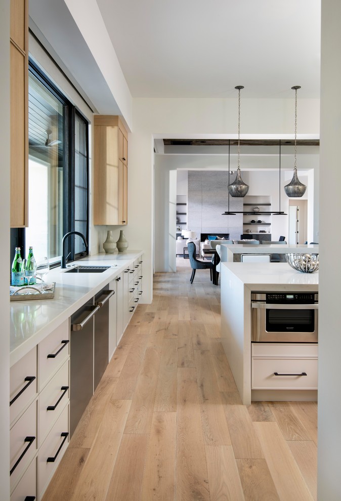Moderne Küche mit hellen Holzschränken, Küchengeräten aus Edelstahl, braunem Holzboden, zwei Kücheninseln, braunem Boden und weißer Arbeitsplatte in Phoenix