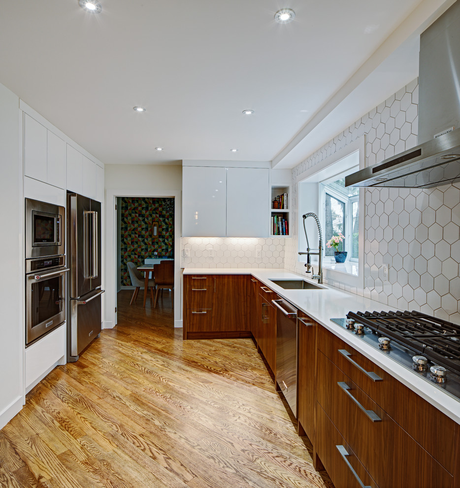 Photo of a contemporary l-shaped kitchen/diner in Toronto with flat-panel cabinets, medium wood cabinets, engineered stone countertops, beige splashback, stainless steel appliances and an island.