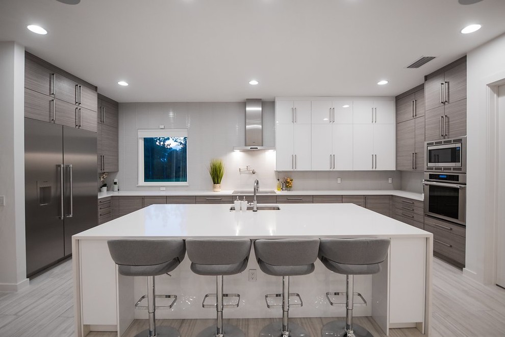 Moderne Küche mit Unterbauwaschbecken, flächenbündigen Schrankfronten, Küchenrückwand in Weiß, Küchengeräten aus Edelstahl, Kücheninsel und weißer Arbeitsplatte in Tampa