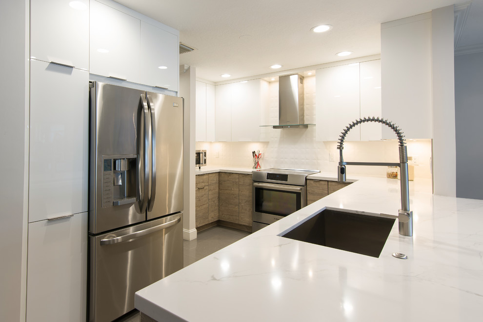 This is an example of a small contemporary u-shaped enclosed kitchen in Miami with a submerged sink, flat-panel cabinets, white cabinets, engineered stone countertops, white splashback, porcelain splashback, stainless steel appliances, a breakfast bar and white worktops.