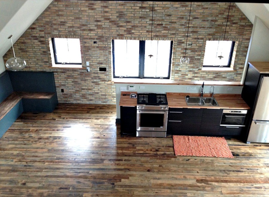 Foto på ett mellanstort industriellt linjärt kök med öppen planlösning, med en dubbel diskho, släta luckor, svarta skåp, träbänkskiva, rostfria vitvaror och mörkt trägolv