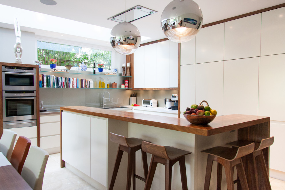 This is an example of a contemporary kitchen/diner in London with flat-panel cabinets, white cabinets, stainless steel appliances and an island.