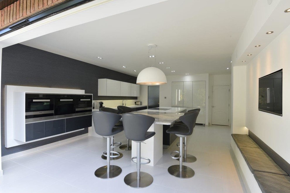This is an example of a large contemporary kitchen/diner in Manchester with an integrated sink, glass-front cabinets, grey cabinets, granite worktops, white splashback, stainless steel appliances, porcelain flooring and an island.