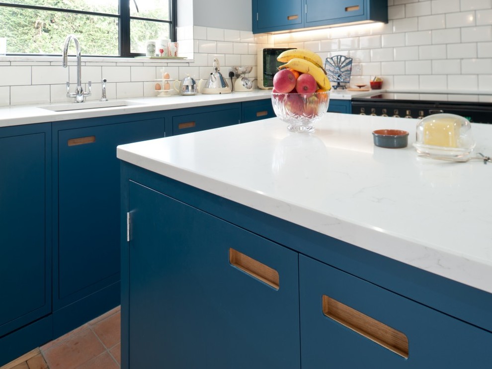 Example of a mid-sized trendy l-shaped eat-in kitchen design in Kent with blue cabinets, white backsplash, ceramic backsplash, white appliances and an island