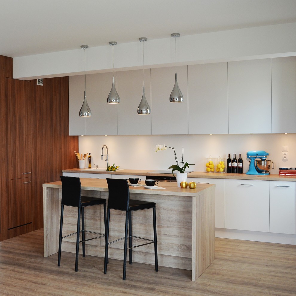Photo of a small contemporary l-shaped kitchen in Other with a built-in sink, flat-panel cabinets, white cabinets, wood worktops, white splashback, integrated appliances, light hardwood flooring, an island and grey floors.