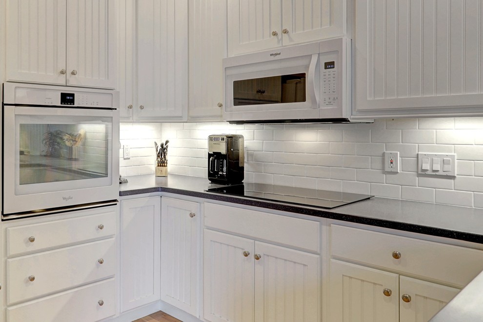 Bild på ett mellanstort maritimt kök, med en enkel diskho, vita skåp, bänkskiva i kvarts, vitt stänkskydd, stänkskydd i tunnelbanekakel, rostfria vitvaror, plywoodgolv, en halv köksö, beiget golv och luckor med upphöjd panel