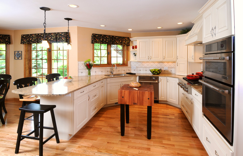 Example of a mid-sized classic u-shaped medium tone wood floor and brown floor eat-in kitchen design in Other with a double-bowl sink, raised-panel cabinets, white cabinets, granite countertops, white backsplash, ceramic backsplash, stainless steel appliances, a peninsula and brown countertops