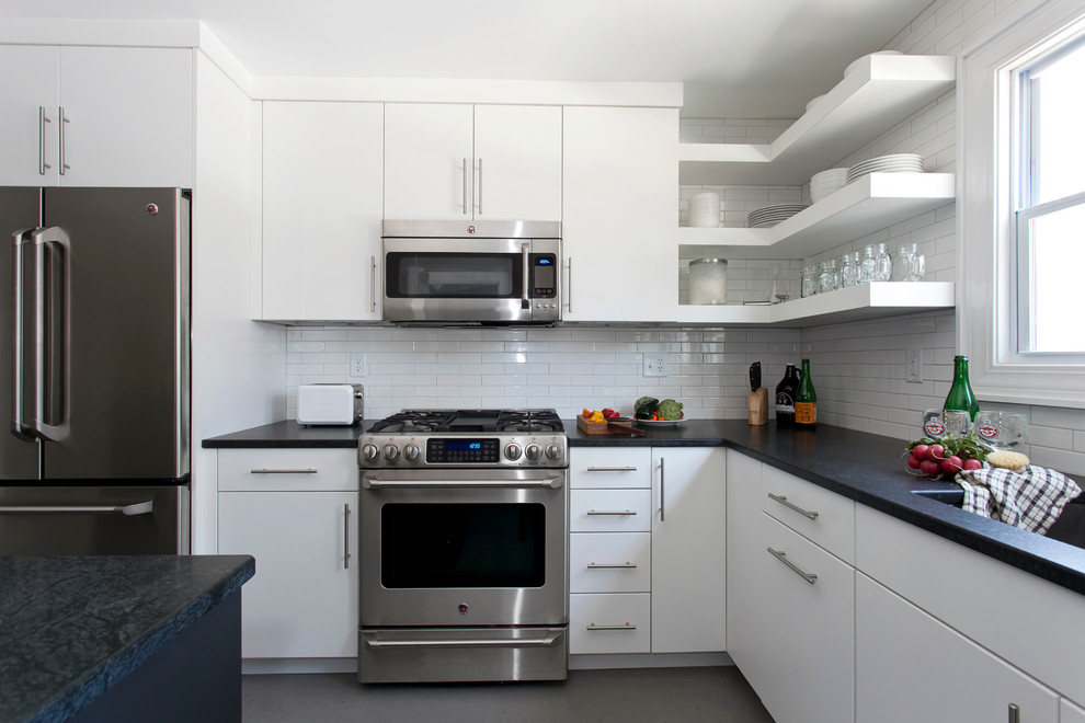 Modern inredning av ett avskilt, litet u-kök, med en undermonterad diskho, vita skåp, vitt stänkskydd, stänkskydd i keramik, rostfria vitvaror, linoleumgolv och en köksö