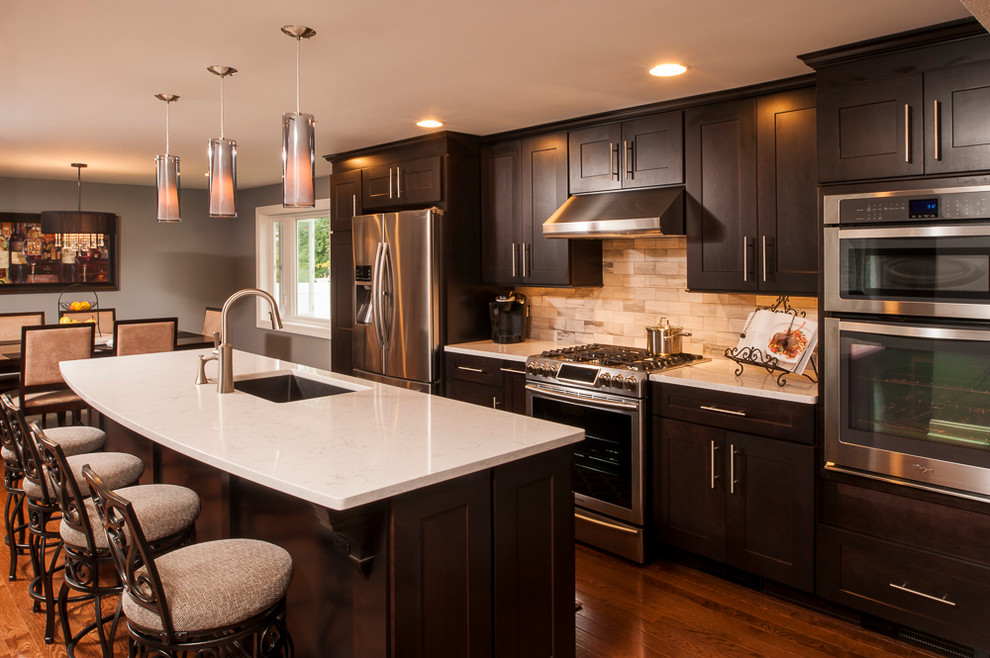 Example of a mid-sized trendy single-wall medium tone wood floor open concept kitchen design in New York with a single-bowl sink, recessed-panel cabinets, dark wood cabinets, quartz countertops, beige backsplash, stone tile backsplash, stainless steel appliances and an island
