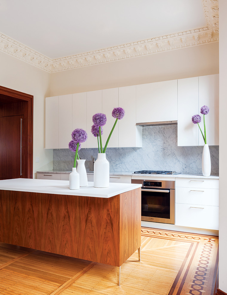 Exempel på ett mellanstort skandinaviskt kök, med en undermonterad diskho, släta luckor, vita skåp, marmorbänkskiva, rostfria vitvaror, mellanmörkt trägolv, en köksö, grått stänkskydd och stänkskydd i sten