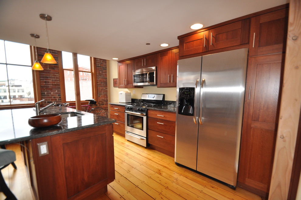 Example of a mid-sized trendy galley light wood floor and beige floor open concept kitchen design in Boston with an undermount sink, shaker cabinets, medium tone wood cabinets, stainless steel appliances, an island, granite countertops and yellow backsplash