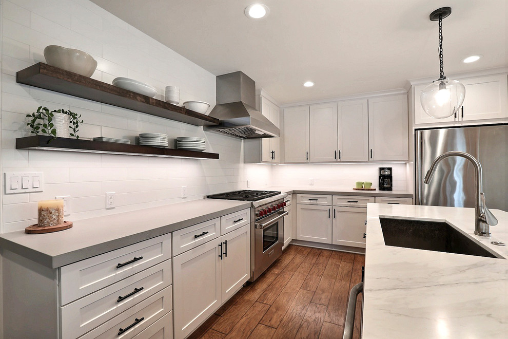 Photo of a medium sized classic l-shaped kitchen/diner in San Francisco with a submerged sink, shaker cabinets, white cabinets, composite countertops, white splashback, ceramic splashback, stainless steel appliances, laminate floors, an island and grey worktops.