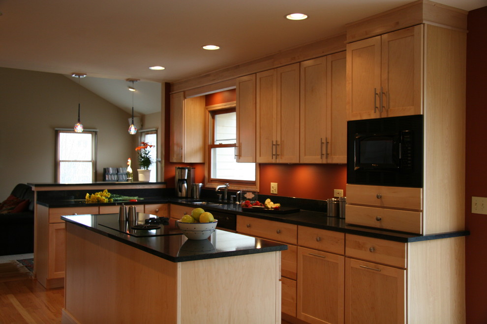 Example of a mid-sized minimalist u-shaped light wood floor eat-in kitchen design in Chicago with an undermount sink, shaker cabinets, light wood cabinets, granite countertops, orange backsplash, black appliances and an island
