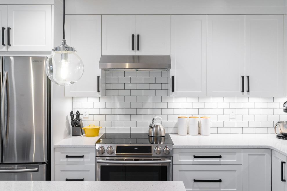 Inredning av ett klassiskt mellanstort vit vitt kök, med en undermonterad diskho, vita skåp, bänkskiva i kvarts, vitt stänkskydd, stänkskydd i tunnelbanekakel, rostfria vitvaror, en köksö, brunt golv, skåp i shakerstil och vinylgolv