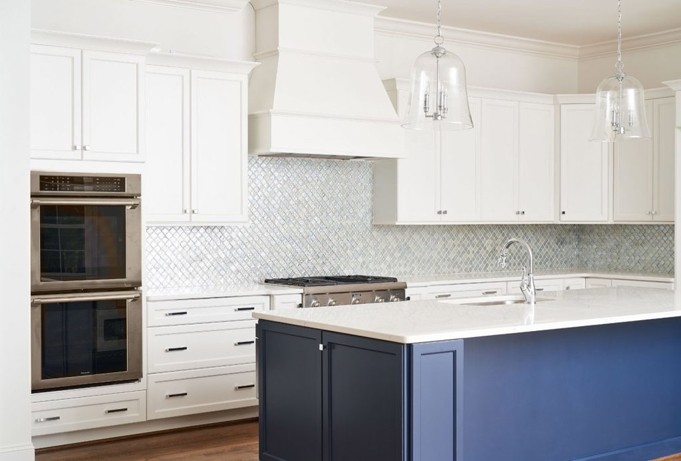 Photo of a medium sized contemporary l-shaped kitchen/diner in Raleigh with a belfast sink, flat-panel cabinets, white cabinets, engineered stone countertops, blue splashback, mosaic tiled splashback, stainless steel appliances, medium hardwood flooring, an island and white worktops.