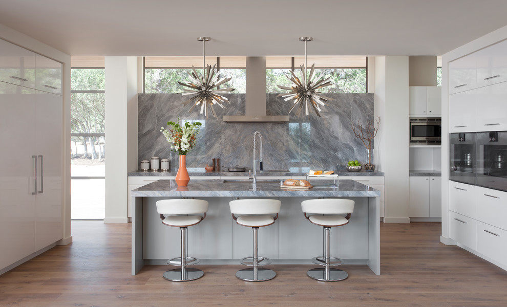Modern inredning av ett grå grått kök, med en undermonterad diskho, släta luckor, vita skåp, grått stänkskydd, stänkskydd i sten, rostfria vitvaror, ljust trägolv, en köksö och beiget golv