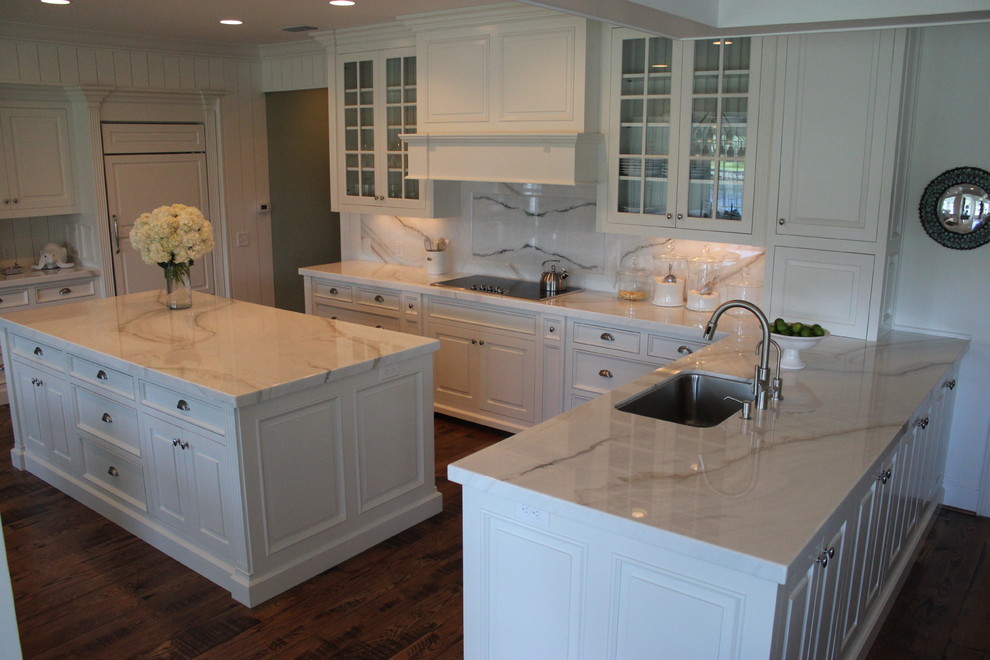 Medium sized beach style u-shaped kitchen pantry in Jacksonville with marble worktops, an island, a submerged sink, raised-panel cabinets, white cabinets, beige splashback, marble splashback, integrated appliances, dark hardwood flooring and brown floors.