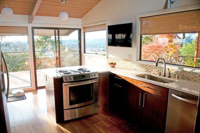 Inredning av ett modernt mellanstort kök, med skåp i mörkt trä, flerfärgad stänkskydd, stänkskydd i glaskakel, rostfria vitvaror, mellanmörkt trägolv och en halv köksö